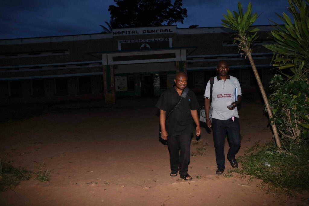 Two healthcare staff walk out of a hospital in the dark.