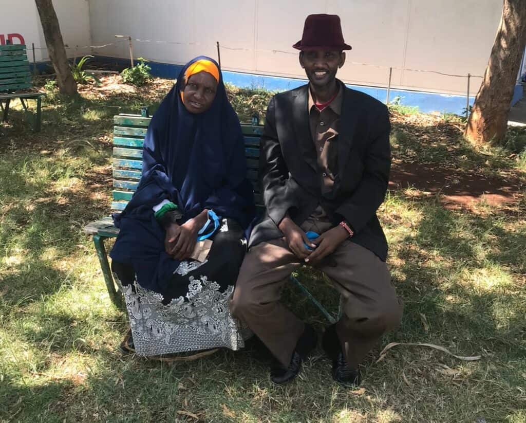 A fistula patient and her husband sit on a bench outside of a treatment facility.