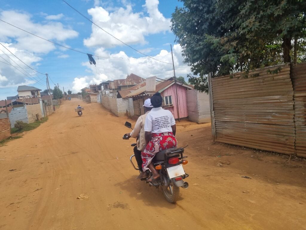 A man and woman ride on a motorcycle down a dirt road.