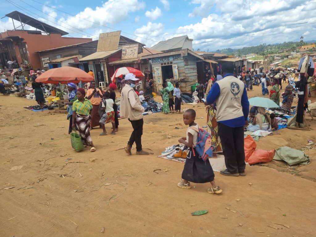 People walk around in a market setting on a dirt road